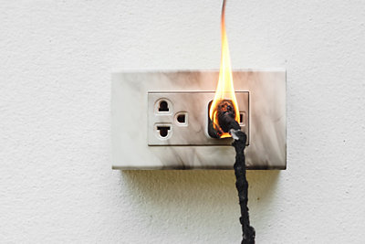 An electrical cord on fire inside of an outlet.