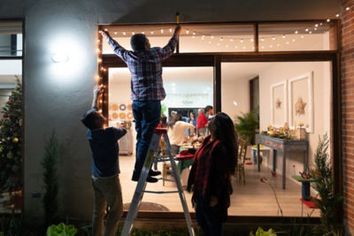Three adults hanging white Christmas lights outside a window