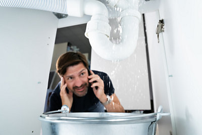 man in his home, seeing a plumbing problem and calling his insurance company