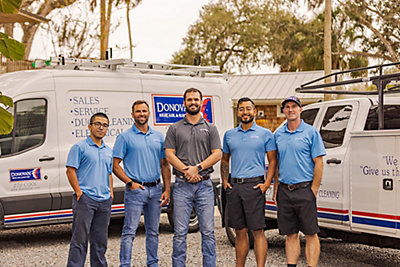 Group of five technicians smiling in front of van and truck