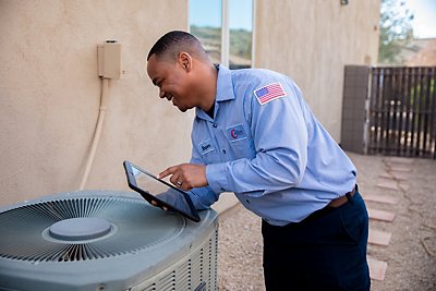 Man leaning over an old HVAC holding an iPad as he prepares to install a new AC system