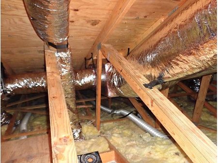 Closeup of exposed insulation and ductwork in an attic.