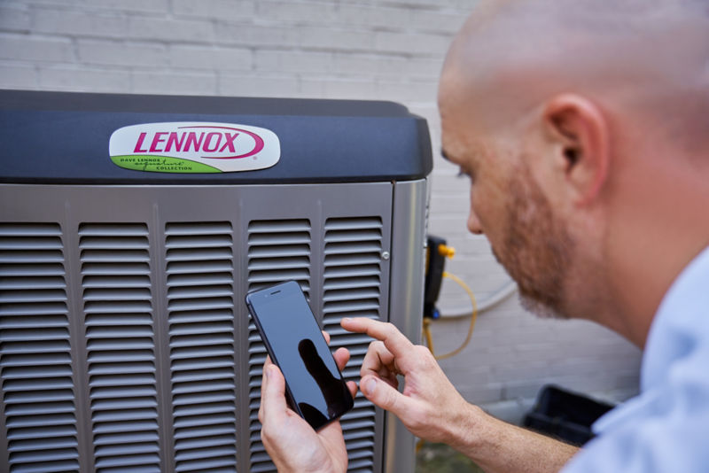HVAC Technician on Phone in Front of Lennox Air Conditioner