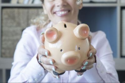 Woman wearing button shirt with blue nails holding a piggy bank