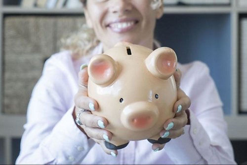 Woman wearing button shirt with blue nails holding a piggy bank