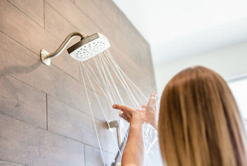 A person washing her hands under a shower head 