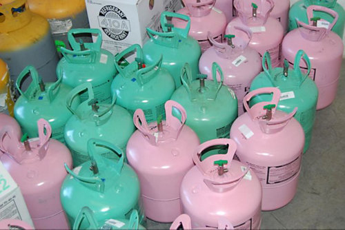 Pink and green gallons of R-410A refrigerant sitting on a floor