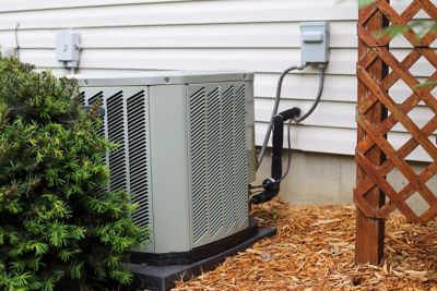 Outdoor component of AC unit hidden behind a bush and lattice