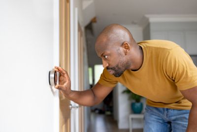 Man standing by thermostat adjusting the temperature