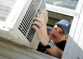 A maintenance technician installing a portable AC unit in a window.