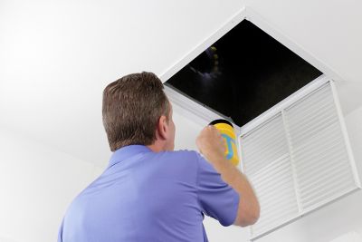 HVAC tech inspecting air duct with flashlight