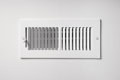 A heating/cooling vent register on the wall of a home, with open/close lever