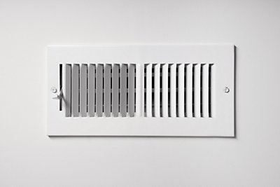 A heating/cooling vent register on the wall of a home, with open/close lever