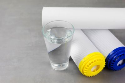 A glass of clean water next to the water purification filter. The concept of a household filtration system.