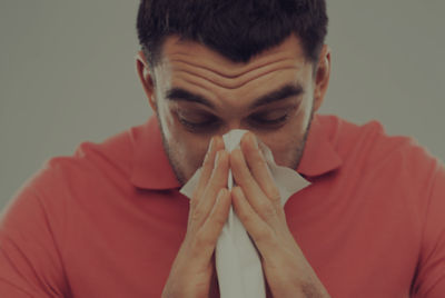 man in red shirt blowing his nose into tissue