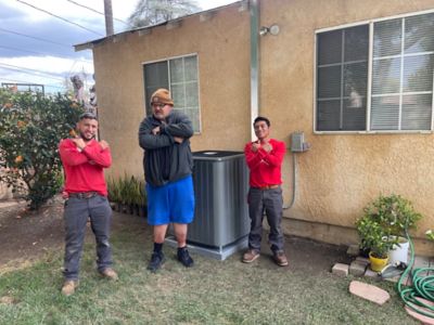 Three people standing in front of AC unit in backyard.