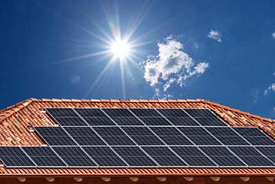Roof with solar panels on blue sky with  sun rays, copy space