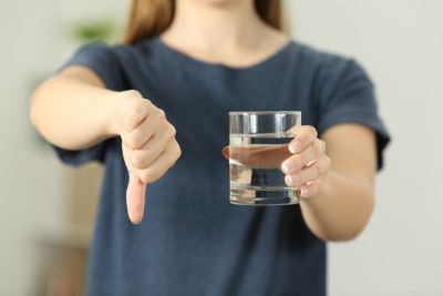 Women holding a cup of water in one hand and making a thumbs down with the other. 