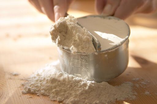 A person pouring flour into a measuring cup