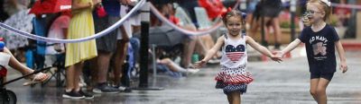 Ava Randazzo, left, and Faith Downing play in the rain before a Fourth of July parade at Market Street, Saturday, July 3, 2021, in The Woodlands.