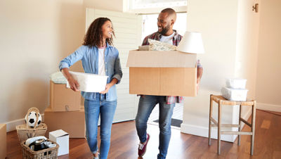 Couple walking carrying boxes smiling at each other