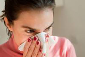 Woman in pink shirt sneezing into tissue