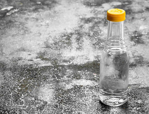 A small clear bottle with a yellow cap sitting on a gray slate.