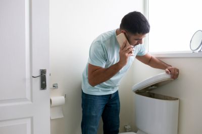 Man standing over a toilet on the phone trying to figure out what the issue is