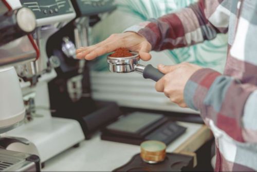 Barista holding an espresso machine part full of espresso grinds