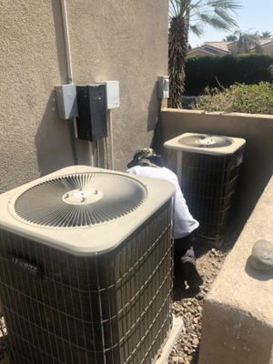 A man fixing an AC unit next to a building.