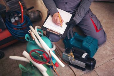 Technician kneeling filling out inspection report on clipboard