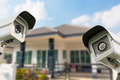 Two floodlight security cameras with home behind them