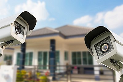 Two floodlight security cameras with home behind them