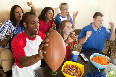 A group of friends with snacks cheering with football in living room