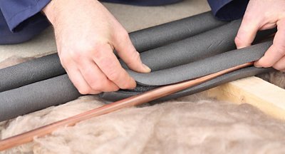 Tech installing insulation onto copper piping