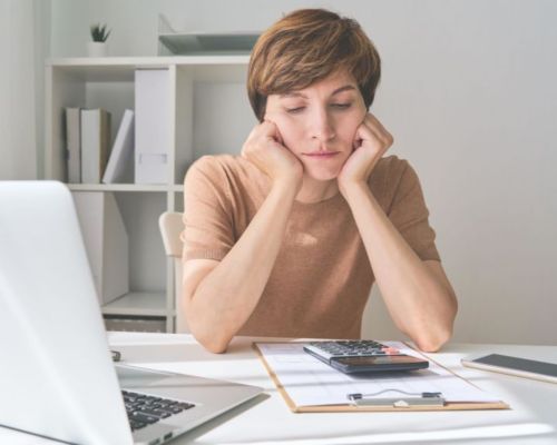 A person sitting at a desk with her hands on her cheeks