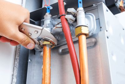 A man's hand tightening the water heater pipes.