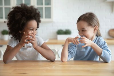 Two girls smiling and drinking water at a table.
