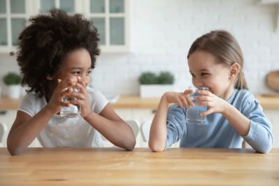 Two girls smiling and drinking water at a table.