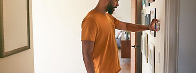 Man wearing an orange t-shirt adjusting his smart thermostat