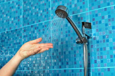 Close-up of a woman's hand check water temperature in the shower with hand shower wall.