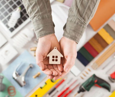 Hands holding a Wooden house ornament over a craft table