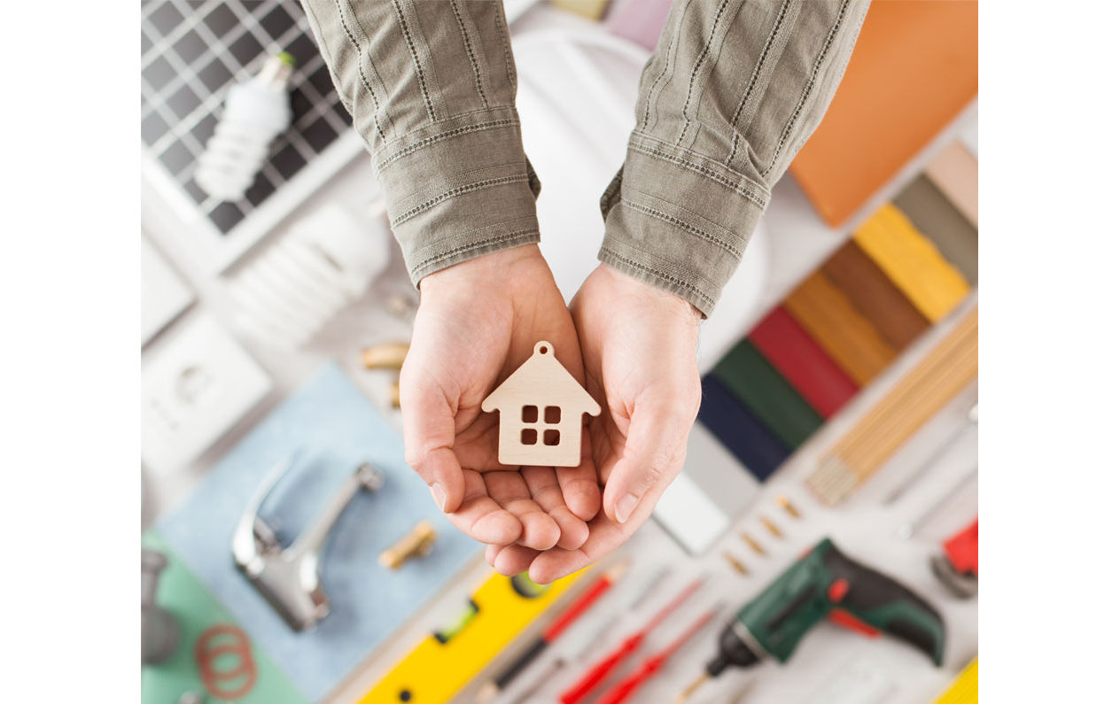 Hands holding a Wooden house ornament over a craft table
