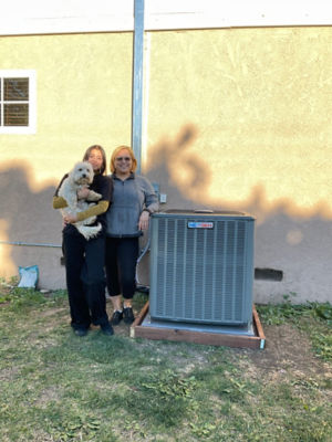 Two women standing side-by-side next to an AC unit.