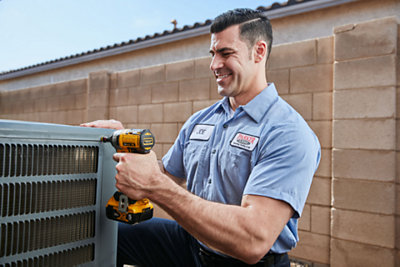 HVAC technician inspecting an outdoor, ground level HVAC unit