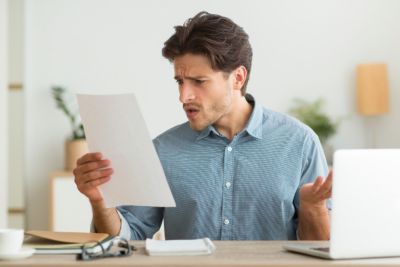 Unexpected Financial Problem. Man Reading Bad News Letter Or Unexpected Tax Notification Indoors.