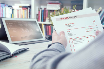 Hands holding invoice in front of tablet at desk