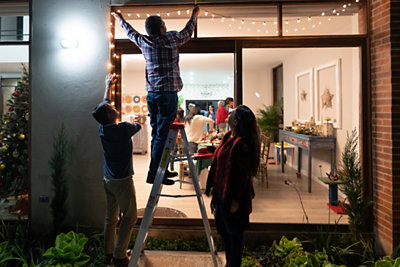 family hanging up holiday lights on their home together