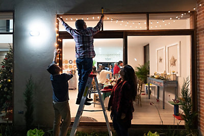 Three adults hanging white Christmas lights outside a window