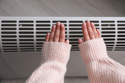 Woman warming hands near electric heater at home